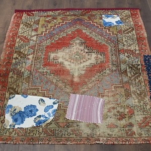 Puede incluir: Una alfombra vintage con un patrón rojo, azul y beige. La alfombra ha sido remendada con retazos de tela en varios patrones, incluyendo diseños florales y a rayas.