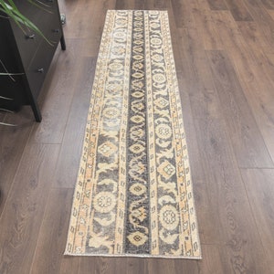 May include: A vintage runner rug with a beige background and intricate black and cream patterns. The rug has a distressed look and is perfect for adding a touch of bohemian style to any room.