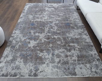 May include: A vintage-style rug with a faded, distressed look. The rug has a light gray background with a subtle blue and brown pattern. The rug has a border with a slightly darker gray color.