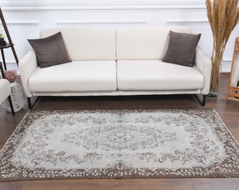 May include: A light brown and white patterned rug with a floral design. The rug is laid out on a wooden floor in front of a white sofa.