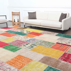 K&ouml;nnte beinhalten: Ein farbenfroher Patchwork-Teppich mit rechteckigen und quadratischen Mustern in Rot-, Gelb-, Gr&uuml;n- und Beiget&ouml;nen. Der Teppich befindet sich in einem Wohnzimmer mit einem wei&szlig;en Sofa und Stuhl.