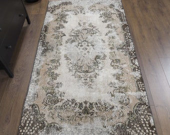 May include: A vintage-style rug with a faded floral pattern in shades of brown, beige, and white. The rug has a distressed look and a worn texture.