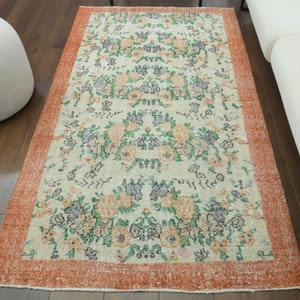 K&ouml;nnte beinhalten: Ein Vintage-Blumenteppich mit cremefarbenem Hintergrund und einem rostfarbenen Rand. Der Teppich zeigt ein sich wiederholendes Muster aus Blumen und Bl&auml;ttern in Gr&uuml;n-, Blau- und Oranget&ouml;nen.