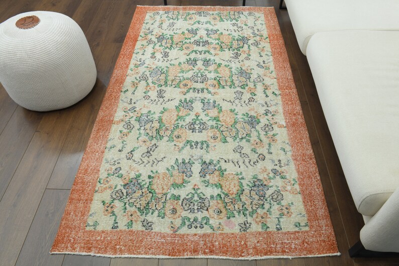 K&ouml;nnte beinhalten: Ein Vintage-Blumenteppich mit cremefarbenem Hintergrund und einem rostfarbenen Rand. Der Teppich zeigt ein sich wiederholendes Muster aus Blumen und Bl&auml;ttern in Gr&uuml;n-, Blau- und Oranget&ouml;nen.