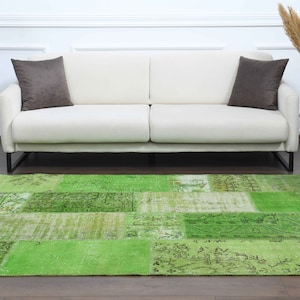 May include: A green patchwork rug with a distressed look, placed in front of a white sofa with brown throw pillows.