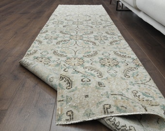 May include: A light grey and beige runner rug with a floral pattern. The rug has a distressed look and is folded in half.