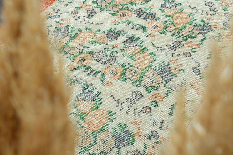 K&ouml;nnte beinhalten: Ein wei&szlig;er Teppich mit einem floralen Muster in Orange-, Gr&uuml;n- und Blaut&ouml;nen. Der Teppich hat einen Vintage-Look und -Feel.