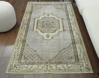 May include: A vintage rug with a light gray background and a beige and brown patterned border. The rug has a central medallion with a geometric design.