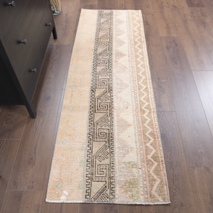 Puede incluir: Una alfombra de pasillo beige con un patrón geométrico marrón. La alfombra tiene un aspecto descolorido y vintage, perfecto para añadir un toque de estilo bohemio a tu hogar.