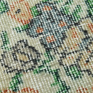 K&ouml;nnte beinhalten: Nahaufnahme eines cremefarbenen Teppichs mit Blumenmuster. Der Teppich zeigt eine Vielzahl von Farben, darunter Gr&uuml;n, Orange und Blau. Der Teppich ist aus einem weichen, gewebten Material gefertigt.