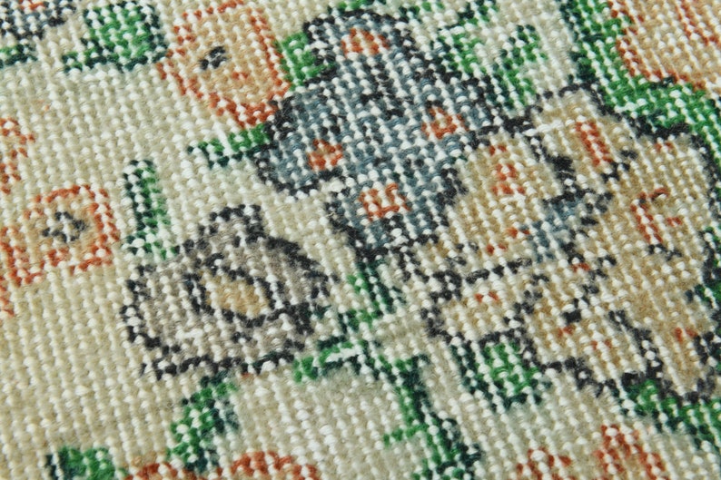 K&ouml;nnte beinhalten: Nahaufnahme eines cremefarbenen Teppichs mit Blumenmuster. Der Teppich zeigt eine Vielzahl von Farben, darunter Gr&uuml;n, Orange und Blau. Der Teppich ist aus einem weichen, gewebten Material gefertigt.