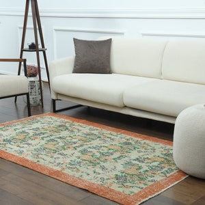 K&ouml;nnte beinhalten: Ein wei&szlig;es Sofa mit einem braunen Kissen steht auf einem Holzboden mit einem gemusterten Teppich. Ein wei&szlig;er Strickhocker steht neben dem Sofa.