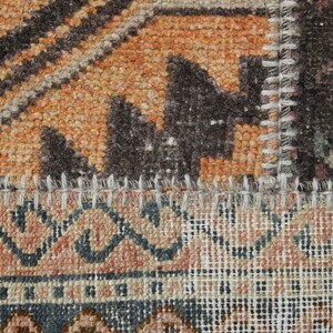 May include: Close-up of a multi-colored woven rug with a stitched seam. The rug has a geometric pattern with shades of brown, orange, and white.