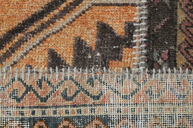 May include: Close-up of a multi-colored woven rug with a stitched seam. The rug has a geometric pattern with shades of brown, orange, and white.