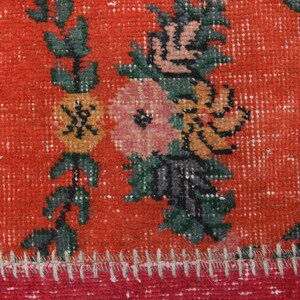 K&ouml;nnte beinhalten: Nahaufnahme eines Abschnitts eines lebendigen, abgenutzten Teppichs. Der Teppich hat einen kr&auml;ftigen roten Hintergrund mit Blumenmustern in Rosa-, Orange- und Gr&uuml;nt&ouml;nen. Die R&auml;nder sind mit einem roten und gelben Besatz versehen, und die N&auml;hte sind sichtbar.