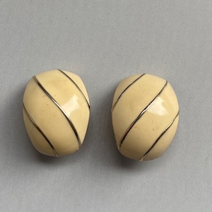May include: A pair of cream-colored clip-on earrings with gold-colored diagonal lines.