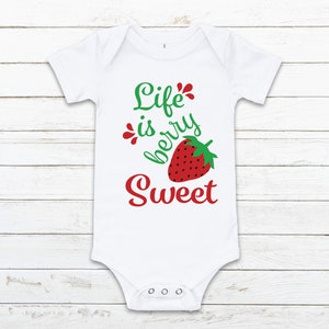May include: White baby onesie with a red strawberry and green leaves. The text "Life is berry sweet" is written in green and red.