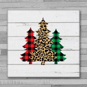 May include: Three Christmas trees on a white wood background. The trees are decorated in red and black plaid, green and black plaid, and leopard print.