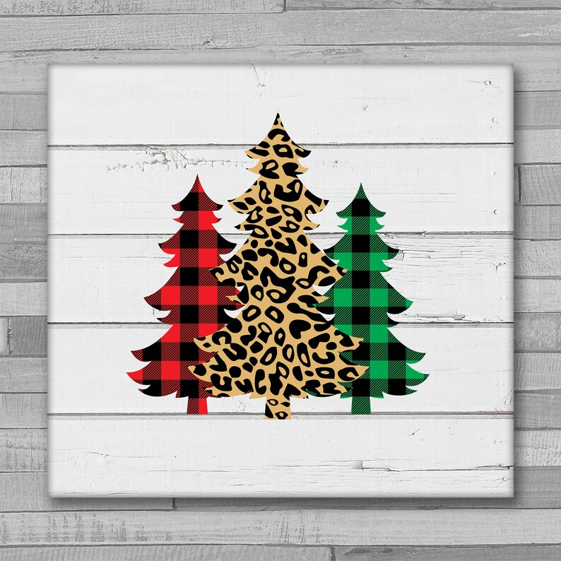 May include: Three Christmas trees on a white wood background. The trees are decorated in red and black plaid, green and black plaid, and leopard print.