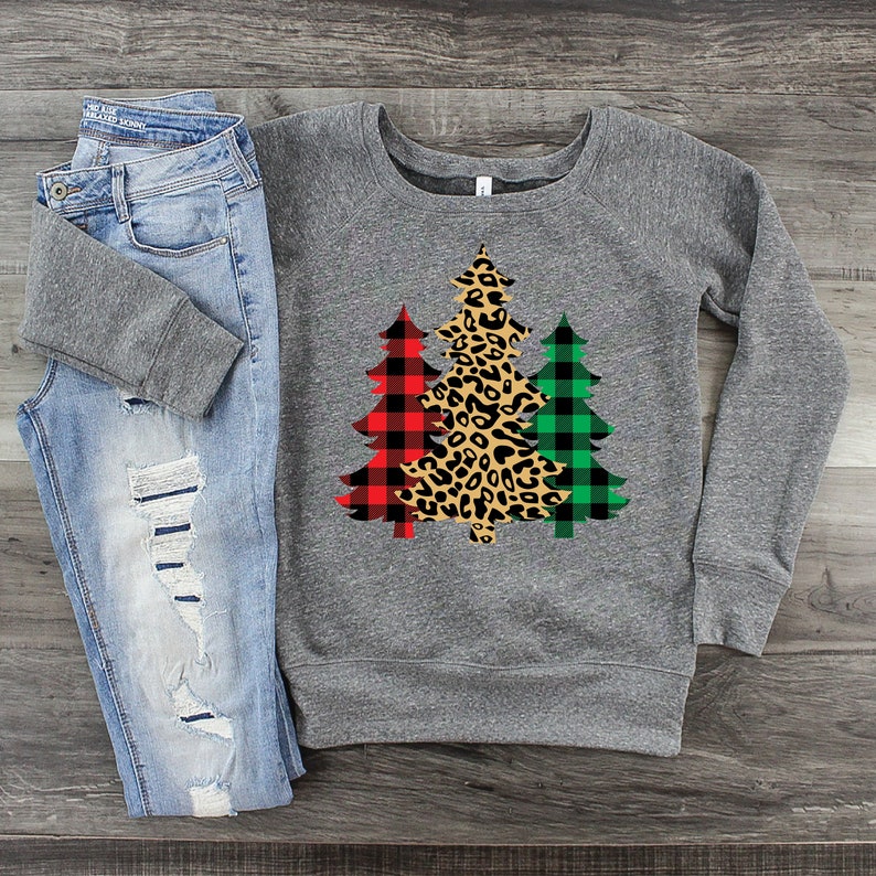 May include: A gray sweatshirt with a design of three Christmas trees. The trees are decorated with red and black buffalo plaid, green and black buffalo plaid, and leopard print.