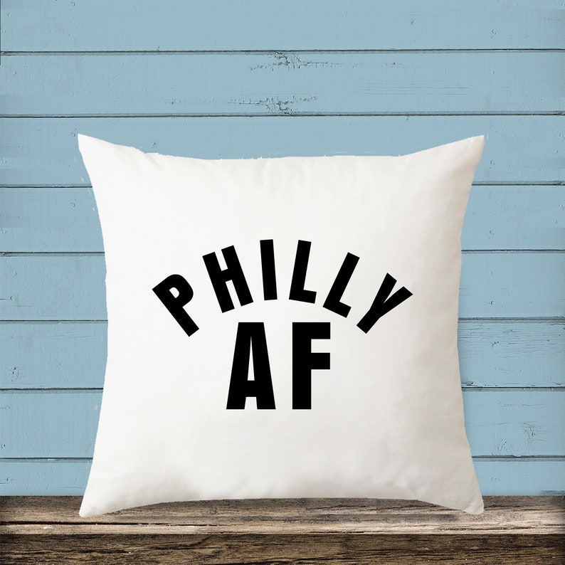 Puede incluir: Almohada blanca con texto negro que dice "Philly AF" en forma de arco redondeado.