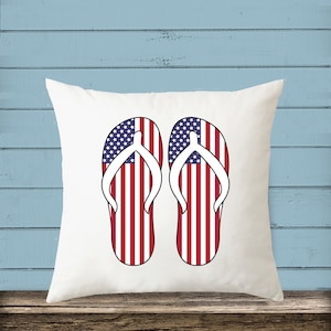 May include: White pillow with a pair of red, white, and blue flip flops printed on it. The flip flops are designed to look like the American flag.