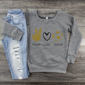 May include: Gray sweatshirt with a peace sign, heart, and soccer ball graphic. The text "Peace Love Soccer" is printed below the graphic.