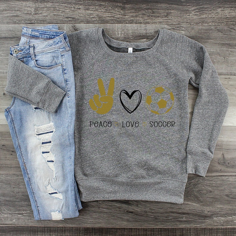 May include: Gray sweatshirt with a peace sign, heart, and soccer ball graphic. The text "Peace Love Soccer" is printed below the graphic.