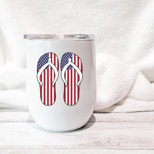 May include: White stainless steel tumbler with a red, white, and blue American flag design on a pair of flip flops.