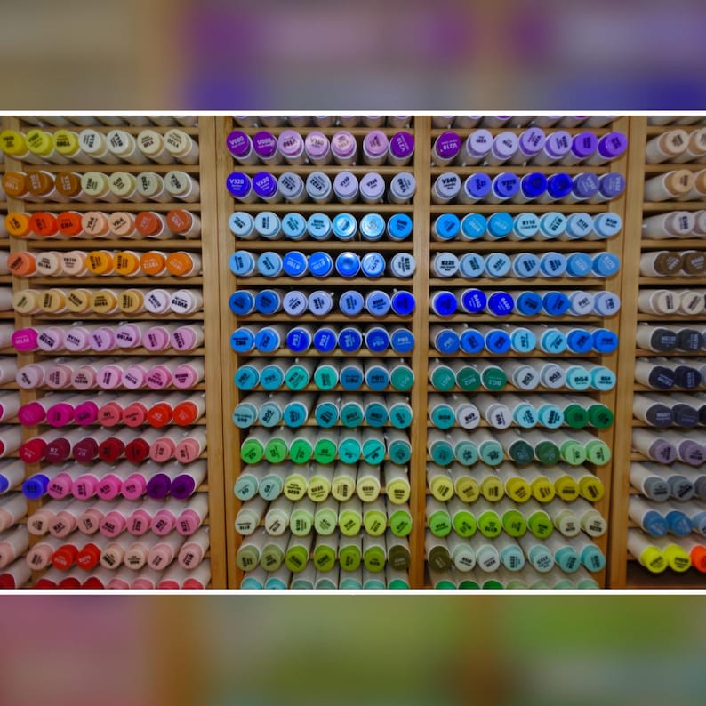 Puede incluir: Un expositor de madera lleno de filas de rotuladores de colores. Los rotuladores est&aacute;n organizados por color, con una amplia gama de tonos visibles, incluyendo rojos, azules, verdes y amarillos. Se ven las tapas de los rotuladores.