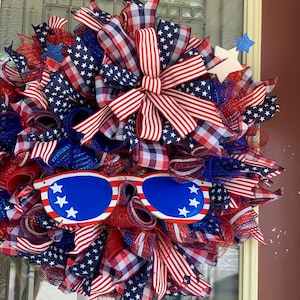 May include: A red, white, and blue patriotic wreath with a large bow, stars, and a pair of blue sunglasses with white stars.