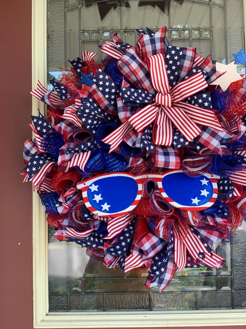 May include: A red, white, and blue patriotic wreath with a red, white, and blue checkered bow and a pair of blue sunglasses with white stars.