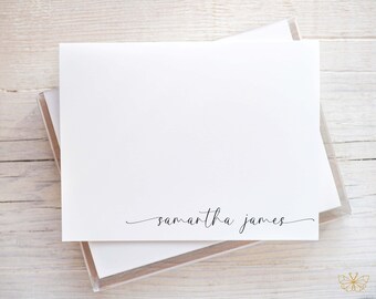 May include: A stack of white stationery cards with the name "samantha james" printed in a delicate, cursive font. The cards are in a clear plastic box, resting on a light wood surface.