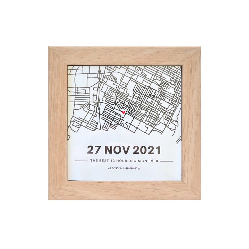 May include: A framed print with a map of a city and a red heart marking a location. The print includes the date "27 NOV 2021" and the text "THE BEST 13 HOUR DECISION EVER" with the coordinates "44.5033&deg; N / 88.0640&deg; W".