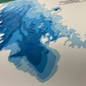 Puede incluir: Un mapa de papel azul y blanco de la regi&oacute;n de la Bah&iacute;a Georgiana de Ontario, Canad&aacute;. El mapa est&aacute; hecho de papel en capas, creando un efecto 3D.