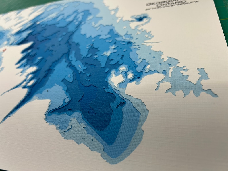 Puede incluir: Un mapa de papel azul y blanco de la regi&oacute;n de la Bah&iacute;a Georgiana de Ontario, Canad&aacute;. El mapa est&aacute; hecho de papel en capas, creando un efecto 3D.