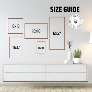 Op de afbeelding: Een maattabel voor ingelijste prints, met verschillende formaten lijsten met afmetingen in inches. De lijsten zijn bruin en worden weergegeven op een witte muur. De tekst "SIZE GUIDE" staat bovenaan de afbeelding.