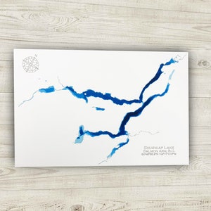 May include: A blue and white watercolor map of Shuswap Lake, Salmon Arm, BC. The map shows the lake's shape and depth with different shades of blue.