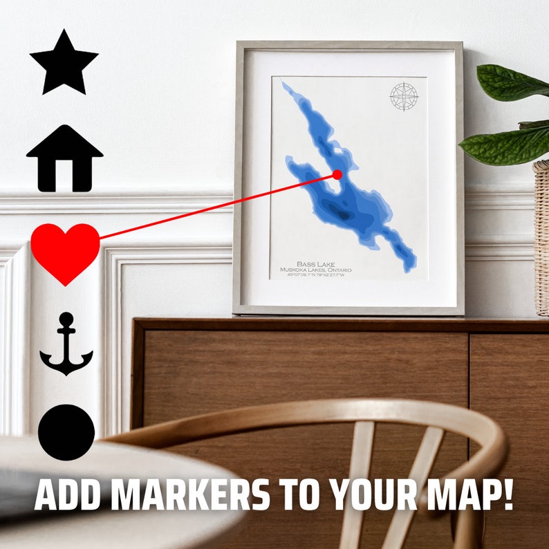 Op de afbeelding: Een ingelijste kaart van Bass Lake, Muskoka Lakes, Ontario, met een rode stip die een locatie op het meer markeert. De kaart is omgeven door een witte passe-partout en een lichtgrijs frame. De afbeelding toont ook pictogrammen in de vorm van een ster, een huis, een hart, een anker en een cirkel.