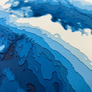 Puede incluir: Arte abstracto de papel con un esquema de color azul y blanco. El papel est&aacute; en capas y cortado para crear un efecto 3D. La obra de arte recuerda a una ola o un oc&eacute;ano.