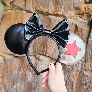 May include: Black and silver Minnie Mouse ears with a red star on the silver ear. The bow is black with a shiny finish.