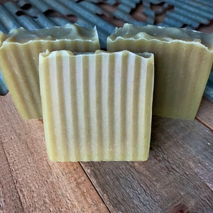 Pode incluir: Três barras de sabonete feitas à mão com um padrão listrado verde e branco. O sabonete está sobre uma superfície de madeira.