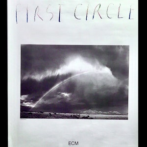 May include: A poster for the Pat Metheny Group's "First Circle" album. The poster features a black and white photograph of a rainbow over a landscape. The band's name and album title are at the top, with band member portraits at the bottom.