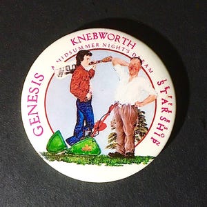 May include: A round pinback button featuring a graphic illustration of two figures, one holding a guitar and the other standing by a green lawnmower. The text reads GENESIS KNEBWORTH A MIDSUMMER NIGHT'S DREAM JEFFERSON STARSHIP in purple lettering.