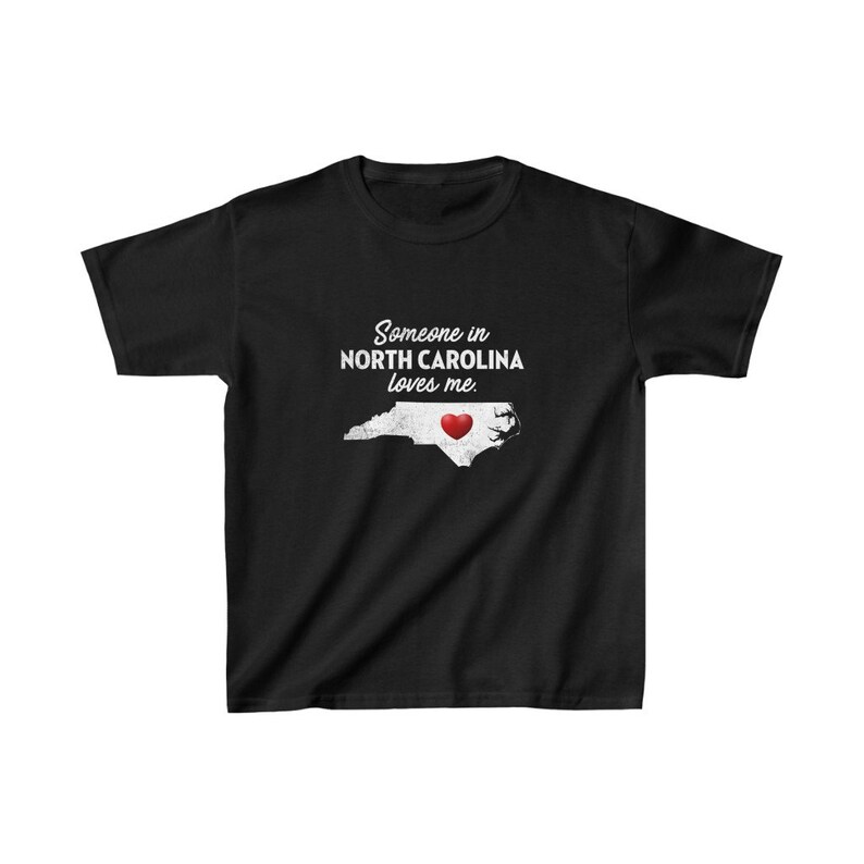 K&ouml;nnte beinhalten: Schwarzes T-Shirt mit wei&szlig;em Text, der "Jemand in North Carolina liebt mich" lautet. Der Text befindet sich &uuml;ber einem wei&szlig;en Umriss des Bundesstaates North Carolina mit einem roten Herzen in der Mitte.