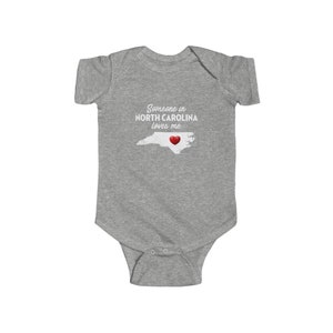 Peut inclure: Combinaison b&eacute;b&eacute; grise avec le texte "Quelqu'un en Caroline du Nord m'aime." et un c&oelig;ur rouge sur un contour blanc de l'&eacute;tat de Caroline du Nord.