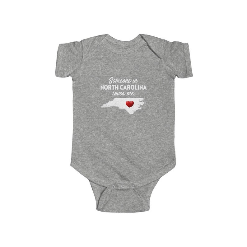 Peut inclure: Combinaison b&eacute;b&eacute; grise avec le texte "Quelqu'un en Caroline du Nord m'aime." et un c&oelig;ur rouge sur un contour blanc de l'&eacute;tat de Caroline du Nord.
