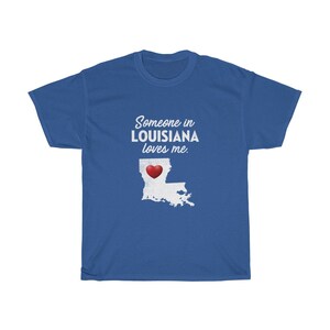 May include: Blue t-shirt with white text that reads "Someone in Louisiana loves me."  A white outline of the state of Louisiana with a red heart in the center is below the text.