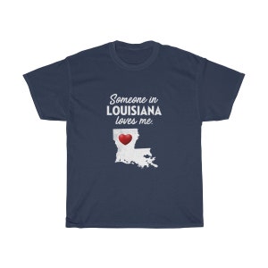 May include: Navy blue t-shirt with white text that reads "Someone in Louisiana loves me."  A white outline of the state of Louisiana with a red heart in the center is below the text.