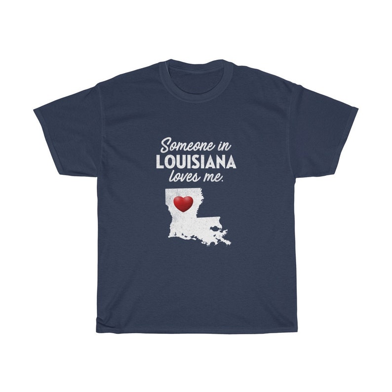 May include: Navy blue t-shirt with white text that reads "Someone in Louisiana loves me."  A white outline of the state of Louisiana with a red heart in the center is below the text.